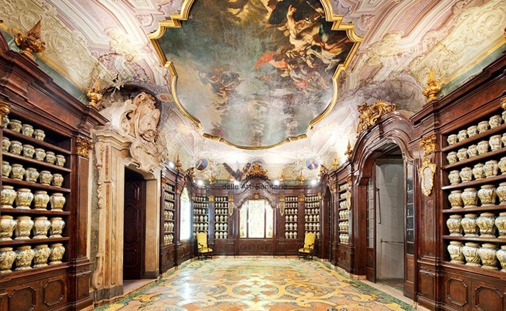 Ornately decorated room with ceramic jars on wooden shelves, frescoed ceiling, and patterned floor.