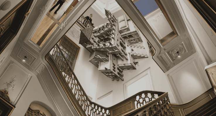 Ornate staircase viewed from below with complex geometric sculpture suspended from a well-lit ceiling.