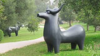 Park with large stylized cow sculptures on a winding pathway amidst trees and greenery.