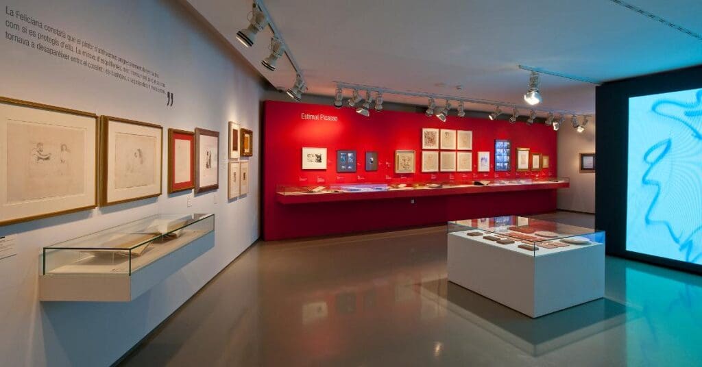 Exhibition room with Picasso artwork, drawings, sketches, and documents in glass displays, bright lighting.