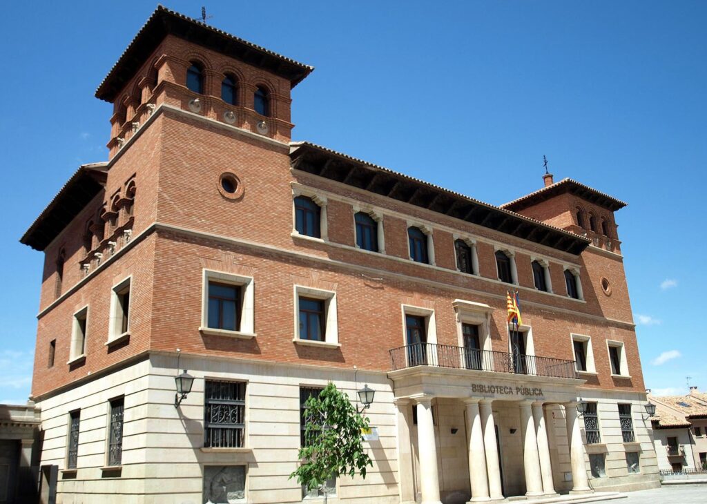 Public library with red brick walls, arched windows, two towers, columns at entrance, clear sky.