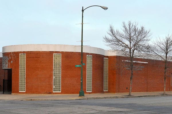 Red brick building with tall windows, curved roof, barren trees, and streetlight at street corner.