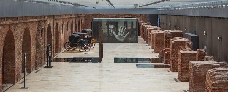 Spacious indoor area with brick arches, old-fashioned carriages, and a large handprint photograph.