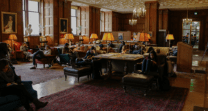 A spacious, elegant study room with people seated on couches and chairs, under warm lighting.