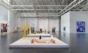 Spacious modern art gallery with high ceilings, exposed beams, contemporary sculptures, and installations