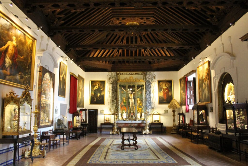 Spacious room with ornate wooden ceiling, large paintings, religious artifacts, and a central crucifix display.