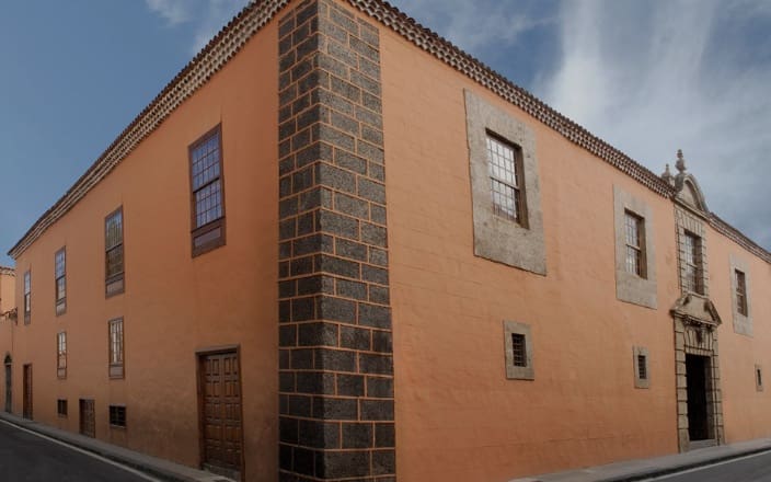 Two-story terracotta building with stone accents, wooden windows, tiled roof, and ornate stone entrance.