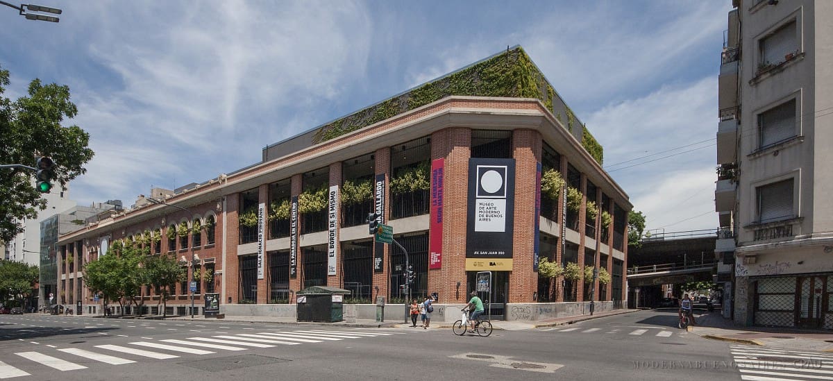Three-story building with vertical gardens, large windows, and banners at corner of urban intersection