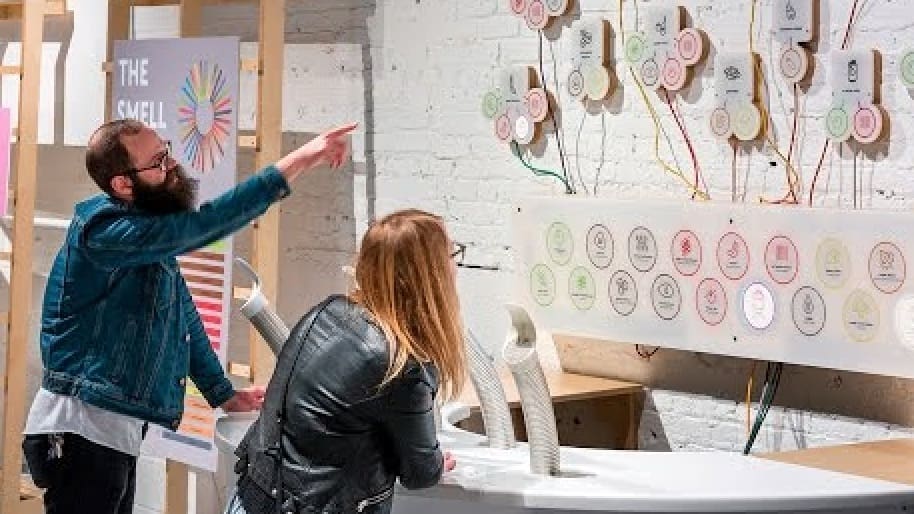 Two people examining a sensory exhibit titled "The Smell" with circular diagrams and colored wires.