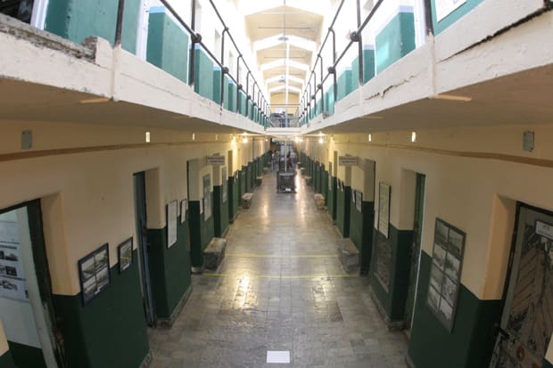 Two-story corridor with green and beige walls, metal railings, photos, arched windows, stone tiles.