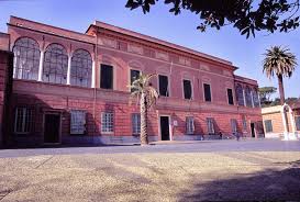 Large, two-story red brick building with arched windows, central door, and palm tree in open space.
