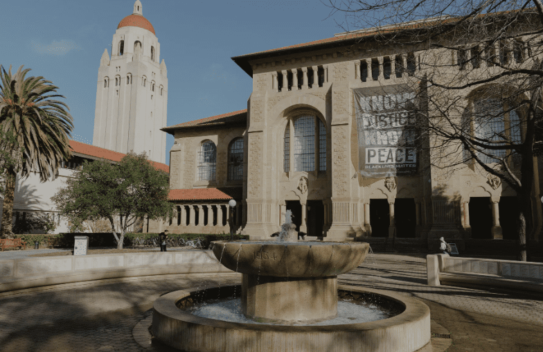 university campus with large building, arched windows, fountain, red-domed tower, trees, benches