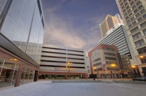 Urban cityscape with office buildings, parking garage, varied architecture, and streetlights.
