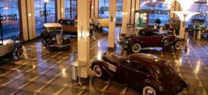 Vintage car showroom with geometric floor, large windows, and classic cars from different eras.