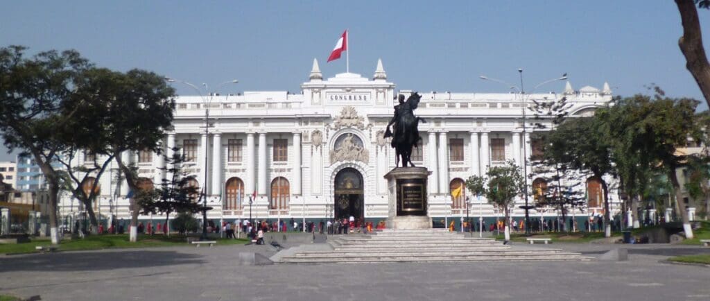 White neoclassical building with columns, a flag on top, and an equestrian statue in front.