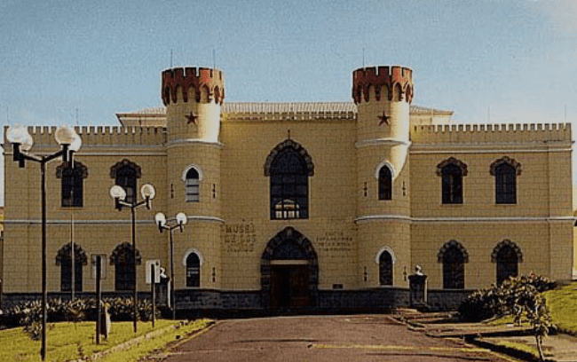 Yellow building, red-topped towers, arched windows, central entrance, stars on towers, light posts.