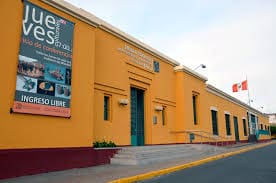 Yellow colonial-style building with cultural event banner, two flags, stairs, and clear sky.