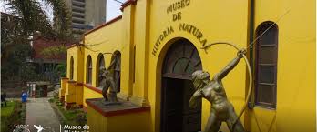 Yellow Museo de Historia Natural with bronze women archers, arched windows, and surrounding trees.