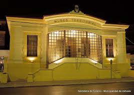 Yellow Museo Territorial building with glass-paneled entrance, Ushuaia, lit up at night.