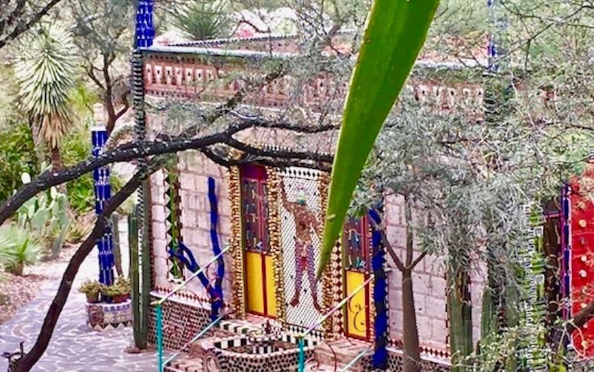 Colorful, intricately designed building with bright tiles and mosaic patterns among trees and desert plants.