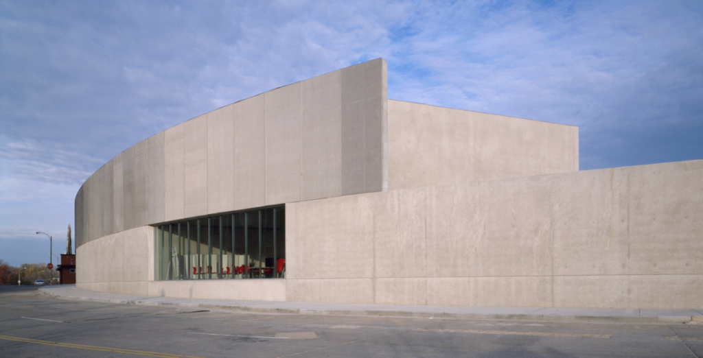 Modern building with a curved concrete exterior, large windows, minimalistic design, and clean lines.