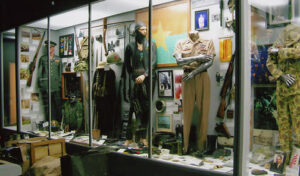 Museum display featuring mannequins in military uniforms, photos, medals, equipment, and artifacts.