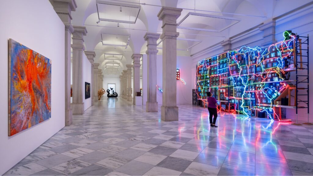 An art gallery with marble floors, abstract paintings, neon light installation of the U.S., and sculptures