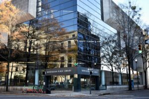 Modern glass-walled Birmingham Public Library reflecting trees and urban surroundings, green traffic light.