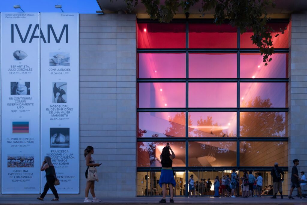 Institut Valencià d'Art Modern facade with exhibition signs, people near entrance with pink reflections.