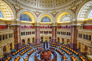 Ornate domed library reading room with arched windows, columns, and circular desk arrangement