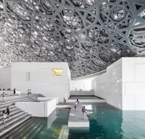 Modern architectural interior with large white cubic structures, shallow water, and geometric ceiling.