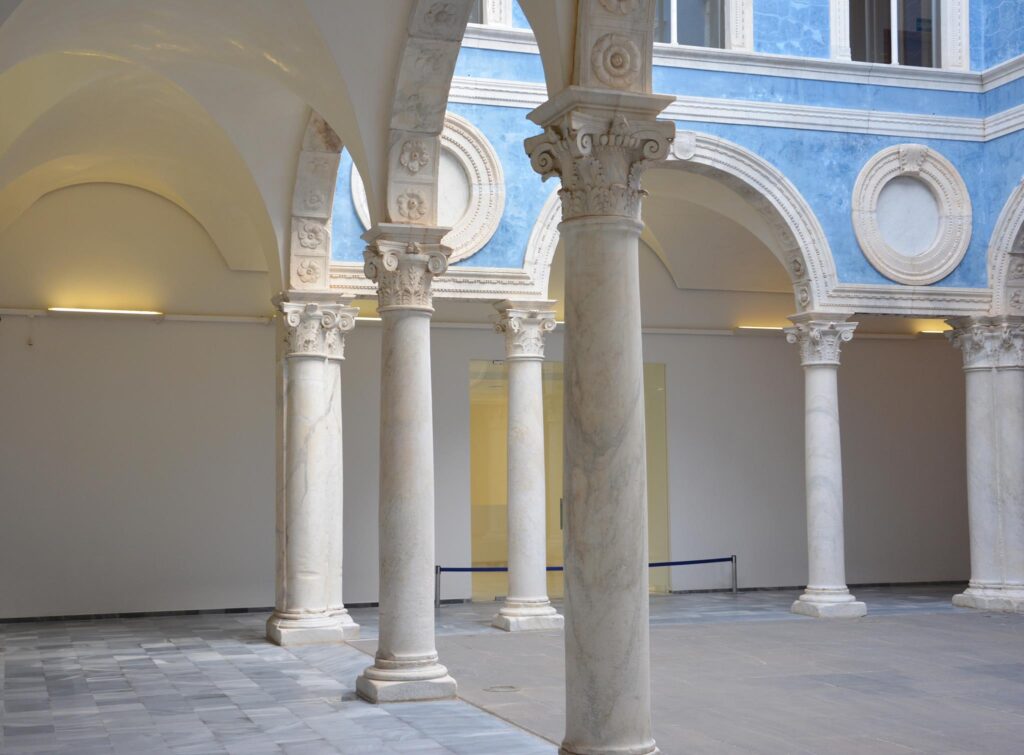 Architectural interior with marble columns, blue painted walls, ornamental details, and geometric tiles.