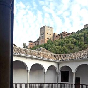 Historic hillside fortress with courtyard featuring white arches, tiled roof, and partly cloudy sky