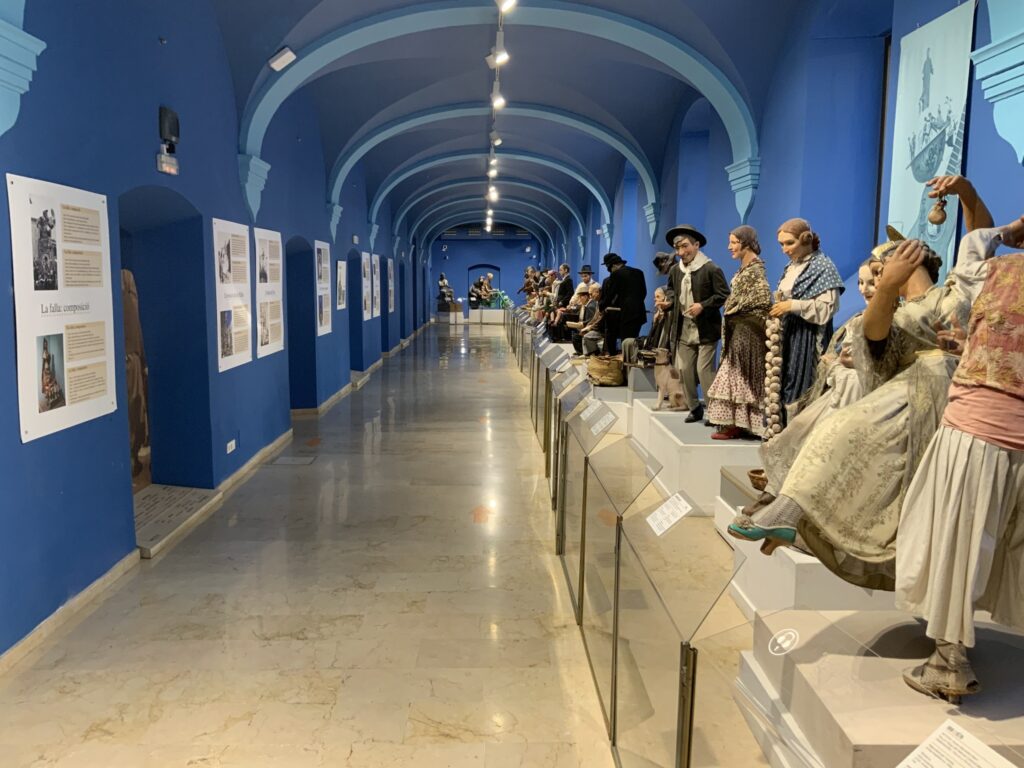 Museum hallway with blue walls, archways, mannequins in traditional clothing, and informational panels.