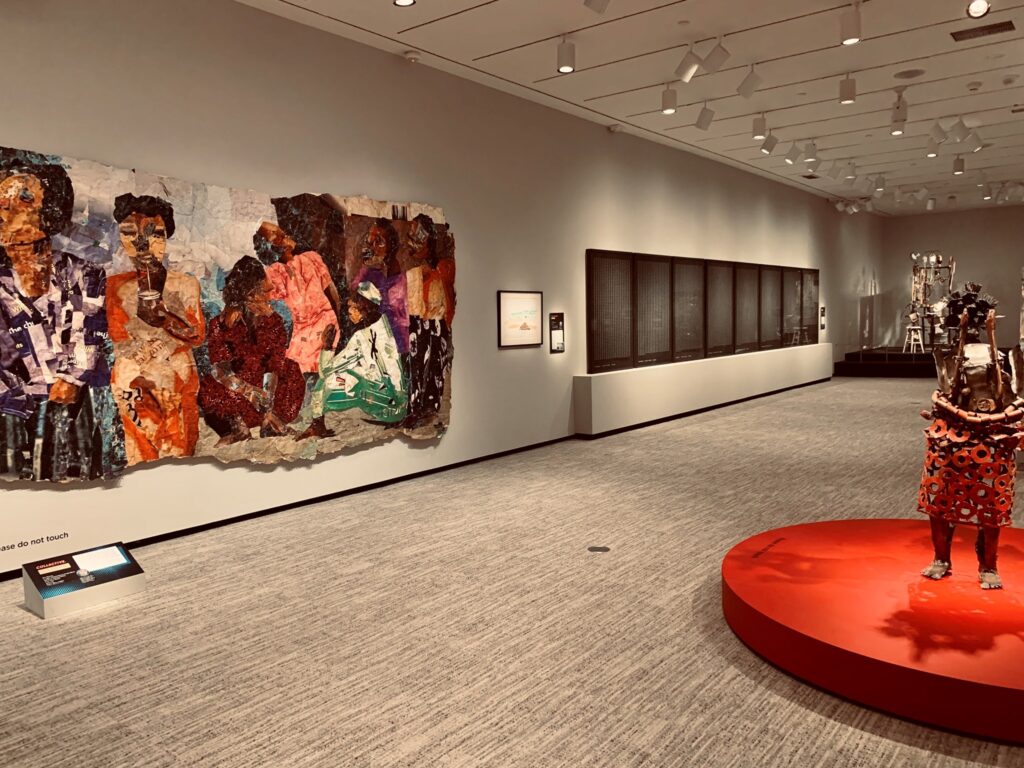 Modern art gallery with a colorful mural, sculpture on red platform, and black-framed wall panels