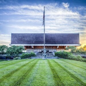 modern building with unique architecture, flagpole, broad neatly mowed lawn, partly cloudy sky