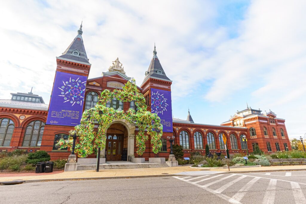 Historic brick building with two towers, arched windows, banners for "Futures" exhibit, green structure.