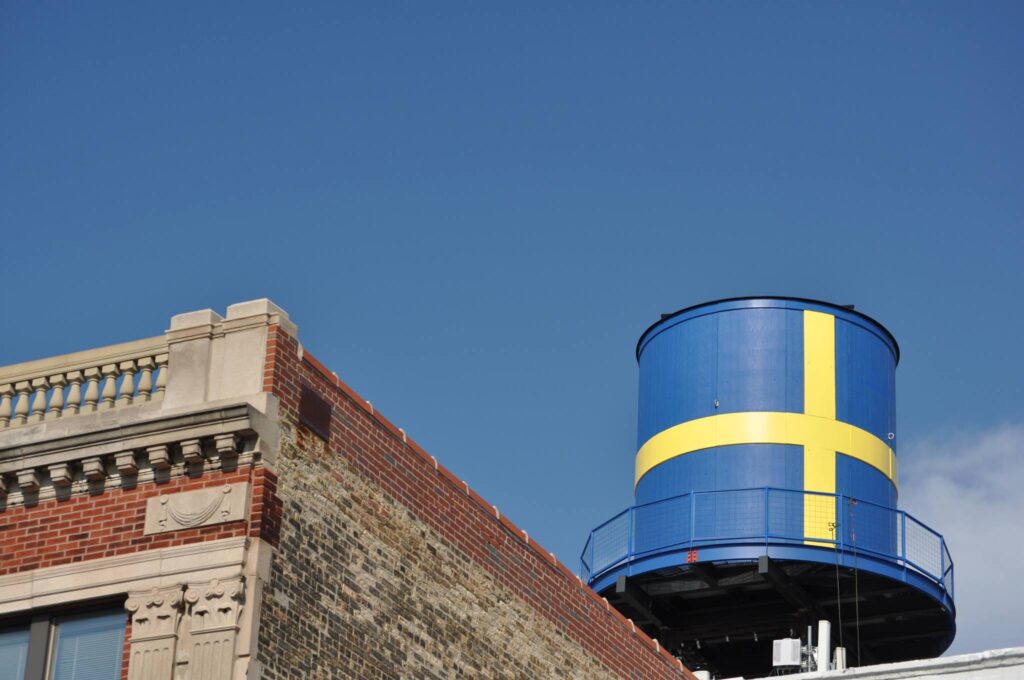 Blue water tower with yellow cross on a brick and ornamental stone building against a clear sky.