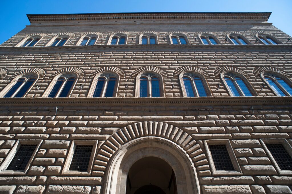 Symmetrical old stone building facade with arched windows and detailed masonry under clear blue sky