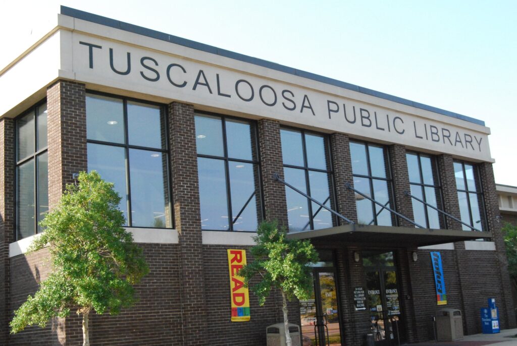 Tuscaloosa Public Library exterior with large windows, brick architecture, trees, and "READ" banners.