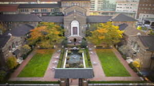 Symmetrical courtyard with fountain, lawns, brick building, arched windows, and autumn trees.