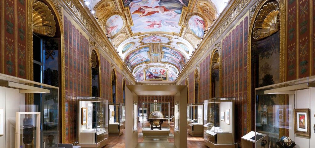 Ornate gallery with painted ceiling, gold accents, display cases, and intricate wall patterns.