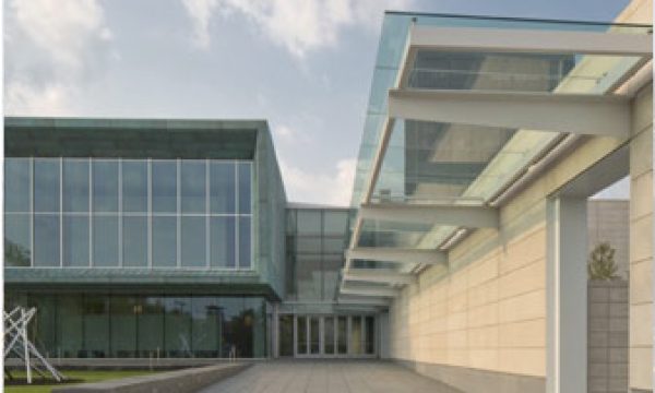 Modern building with large glass windows, overhanging glass canopy, and sleek architectural lines