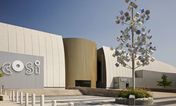 Modern building with curved surfaces labeled "COSI" and a metallic cubic tree sculpture in front.