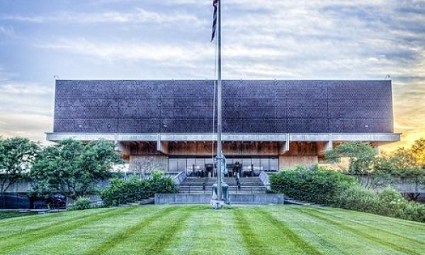 modern building with unique architecture, flagpole, broad neatly mowed lawn, partly cloudy sky